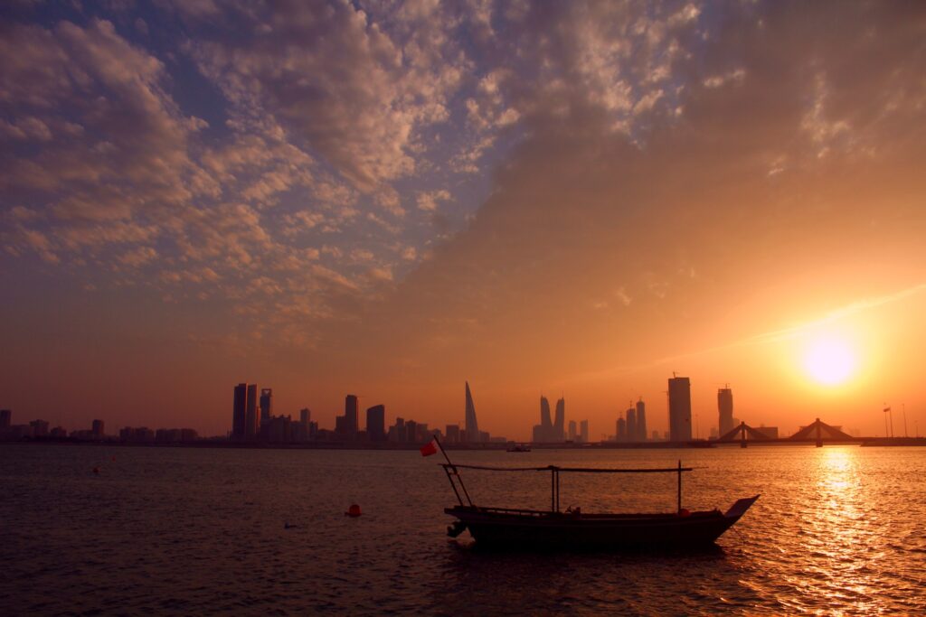 An old ship with Bahrain’s flag in front of the city and the sunset